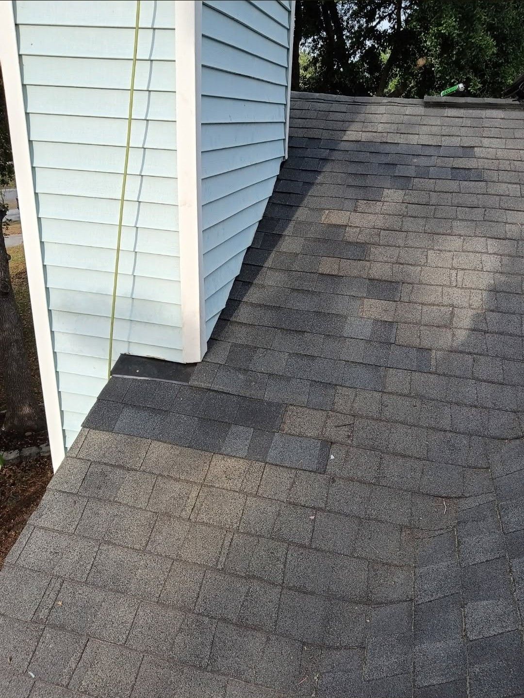 Side of a house with gray shingled roof and white siding, showing roof edge and shadow.