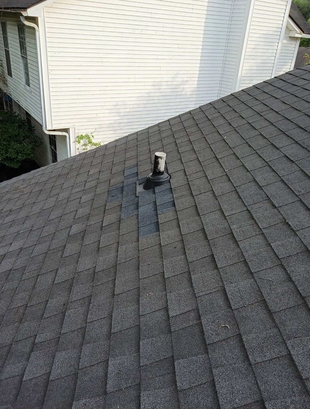 Roof shingle repair vent on gray asphalt roof beside white house siding