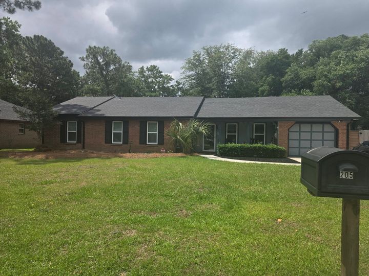Single-story brick house with a green lawn, cloudy sky, and a black mailbox in the foreground
