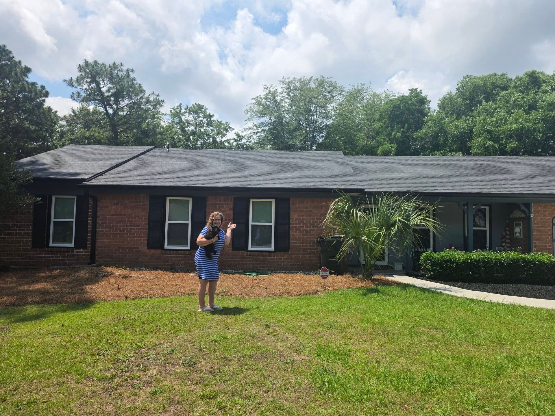 Brick ranch house with a woman standing on the front lawn under cloudy skies