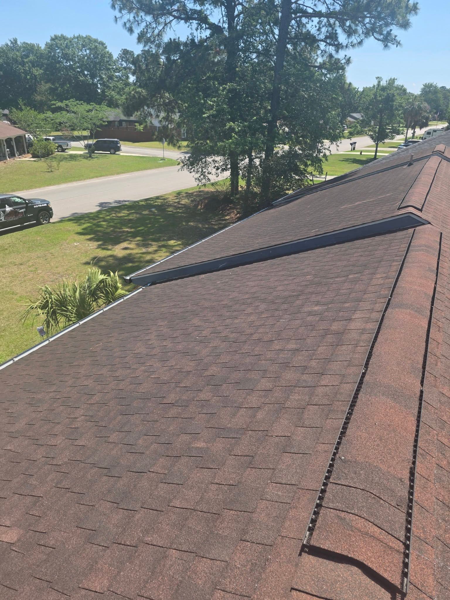 Rooftop with brown shingles overlooking a tree-lined suburban street on a sunny day