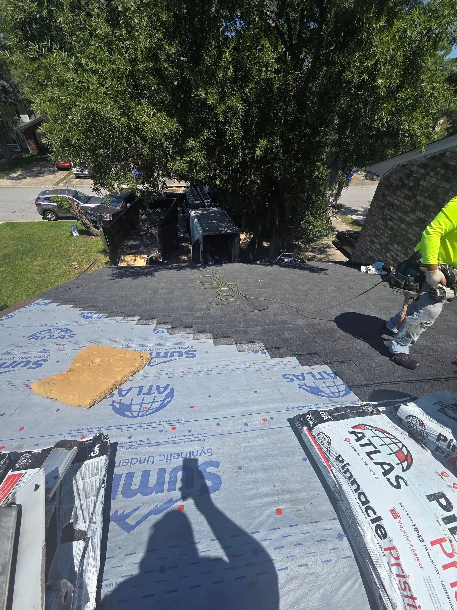 Person on a roof near trees, with tarps and tools laid out in bright sunlight.