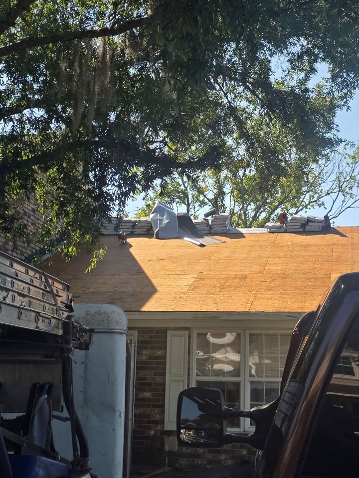 House roof with orange shingles under leafy trees, with a vehicle parked in the foreground.