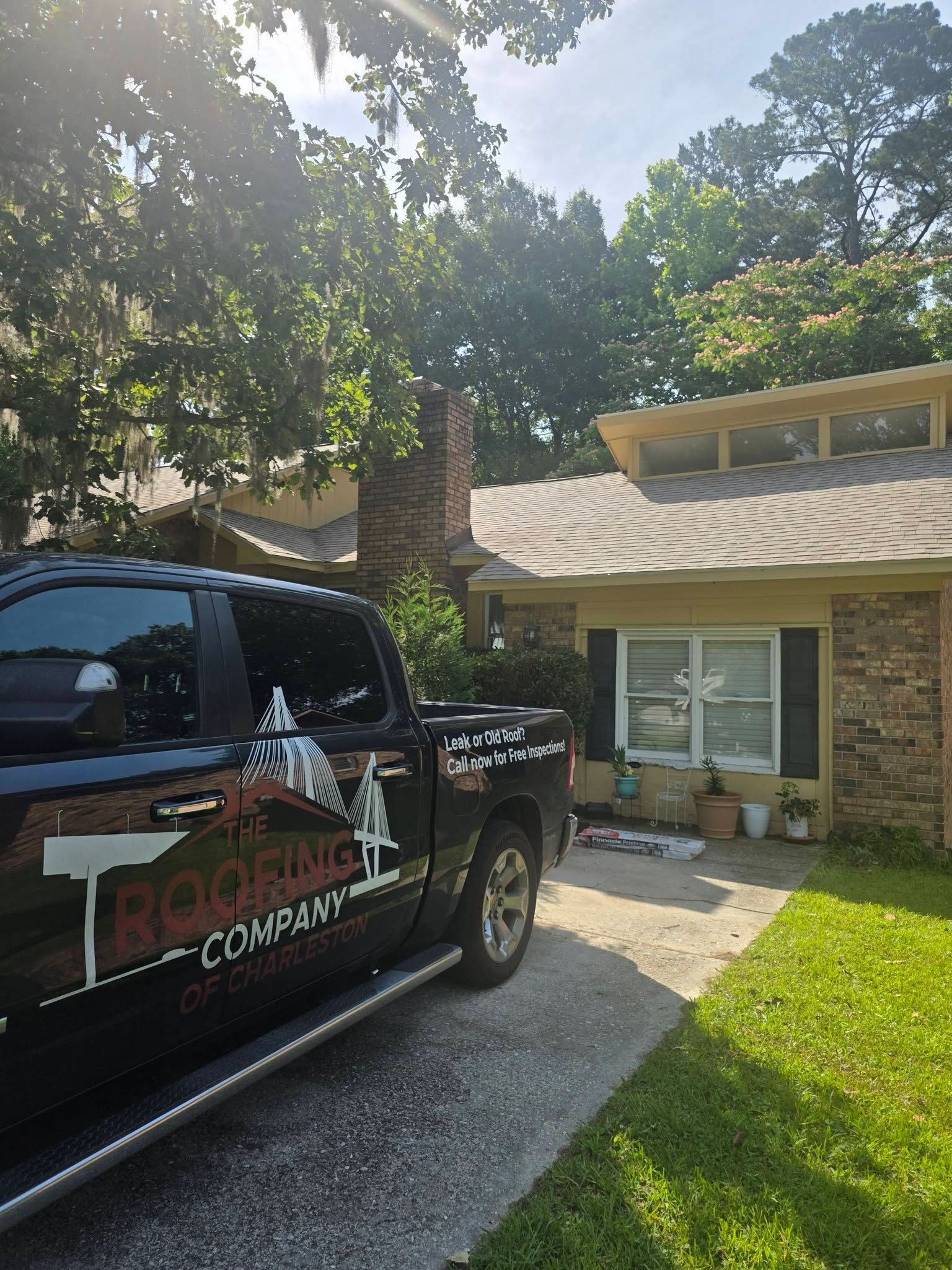 Black pickup truck parked in front of a brick house with a sunlit yard and trees.