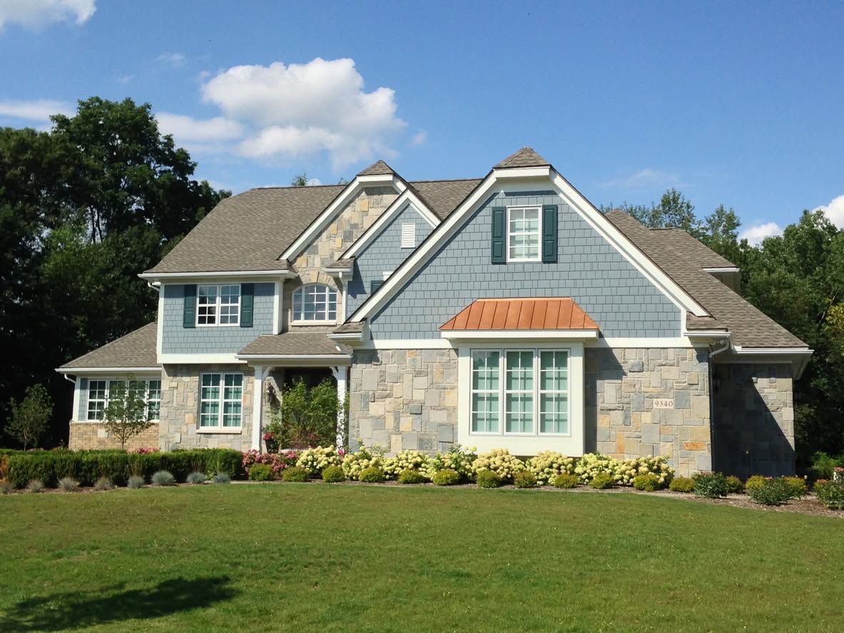 Large gray stone house with blue siding, white trim, and a green lawn under a clear sky