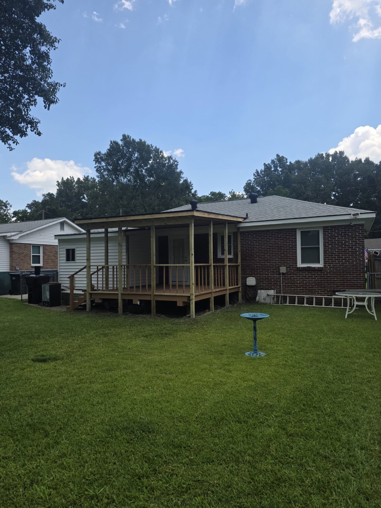 Backyard with a wooden deck attached to a brick house, green lawn, and a birdbath under a cloudy sky