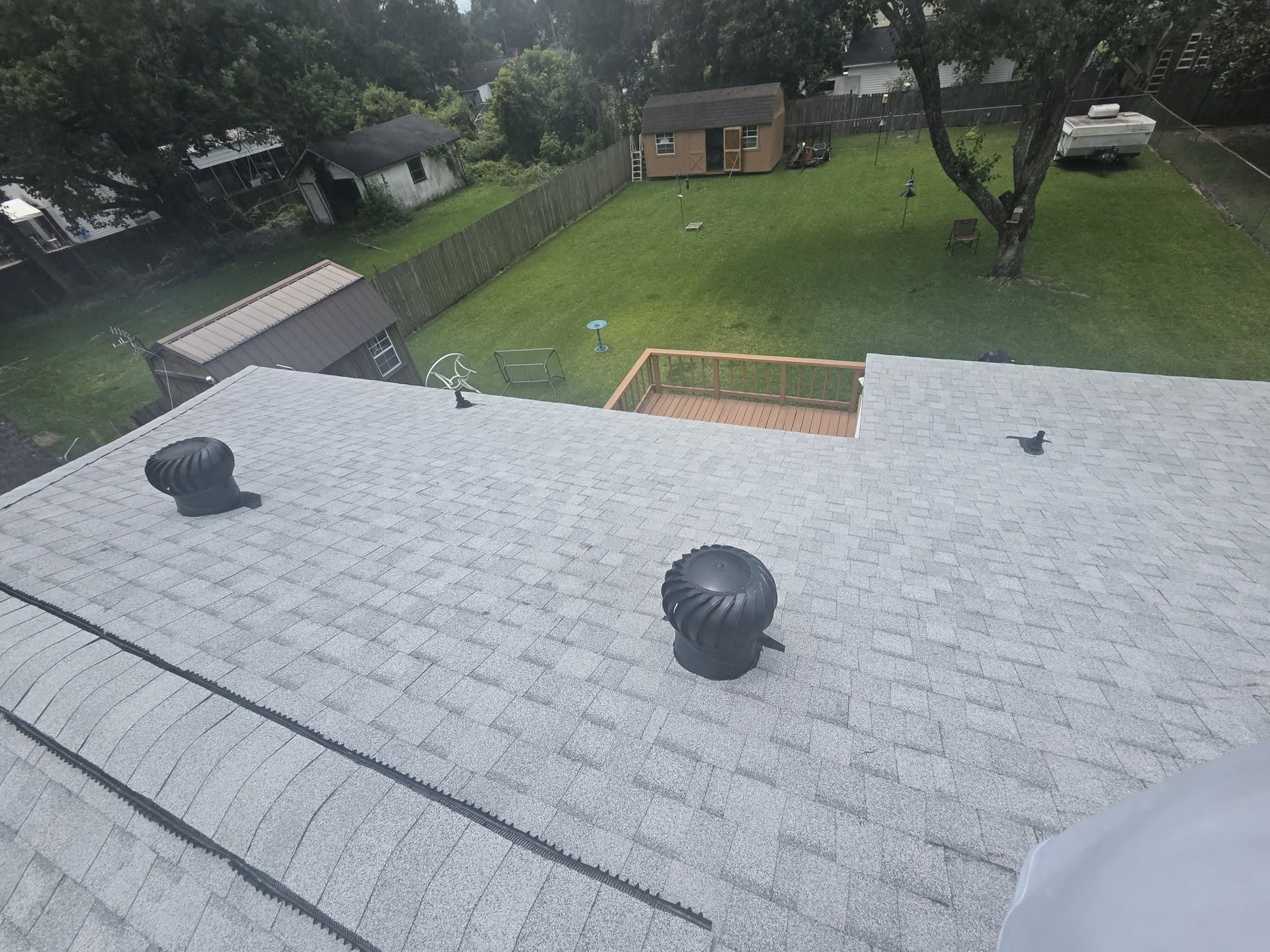 Rooftop view over a backyard with trees, lawn, and a small shed.