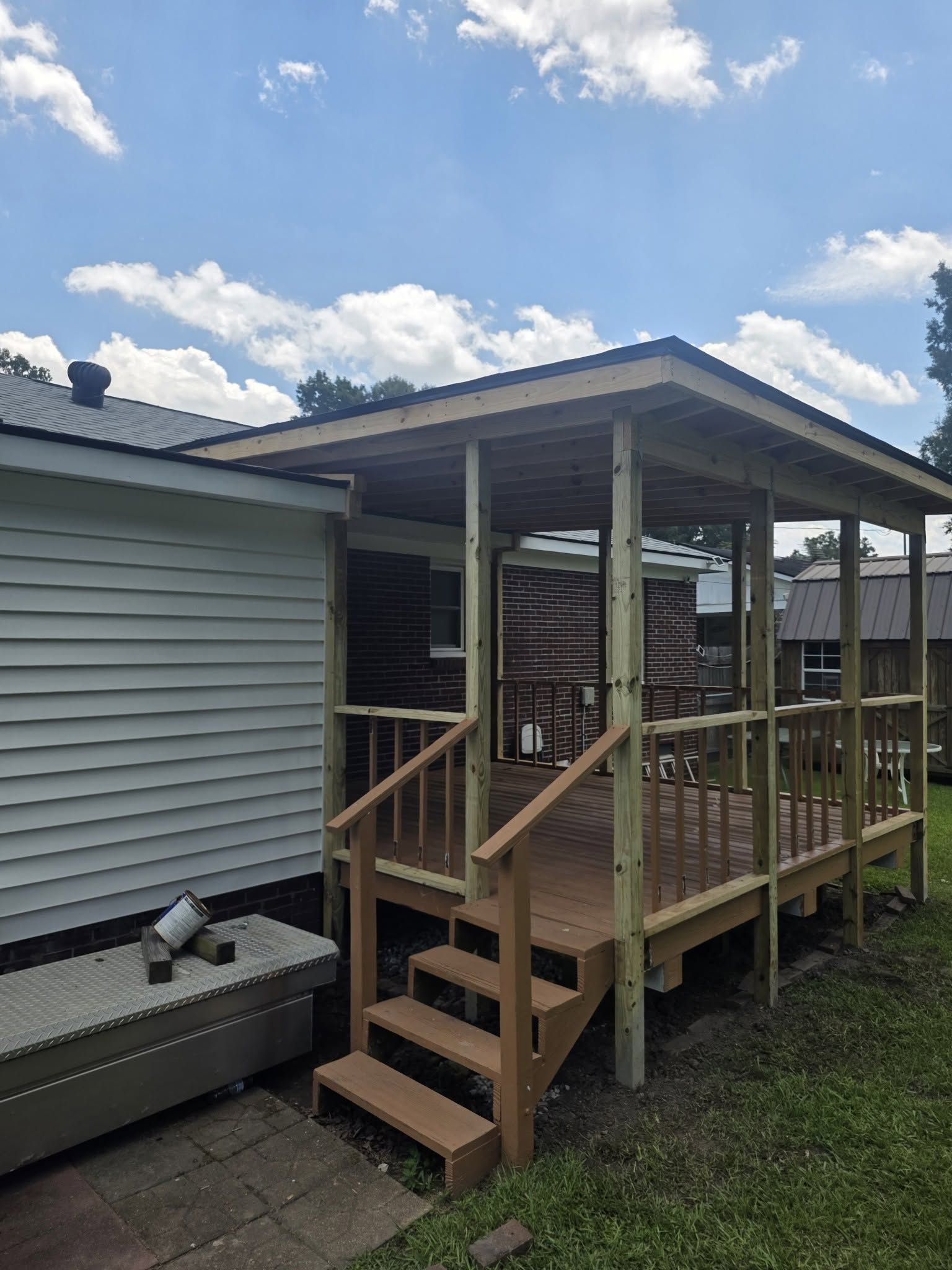 Wooden porch addition with steps and railing beside a house under a cloudy sky