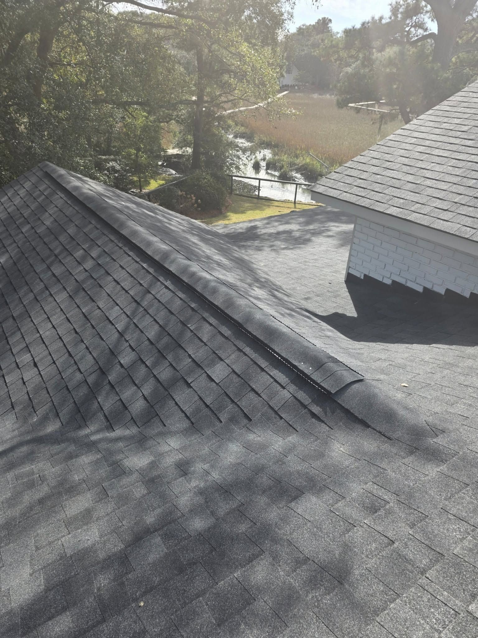 Two shingled rooftops meeting at a valley, with trees and sunlight in the background