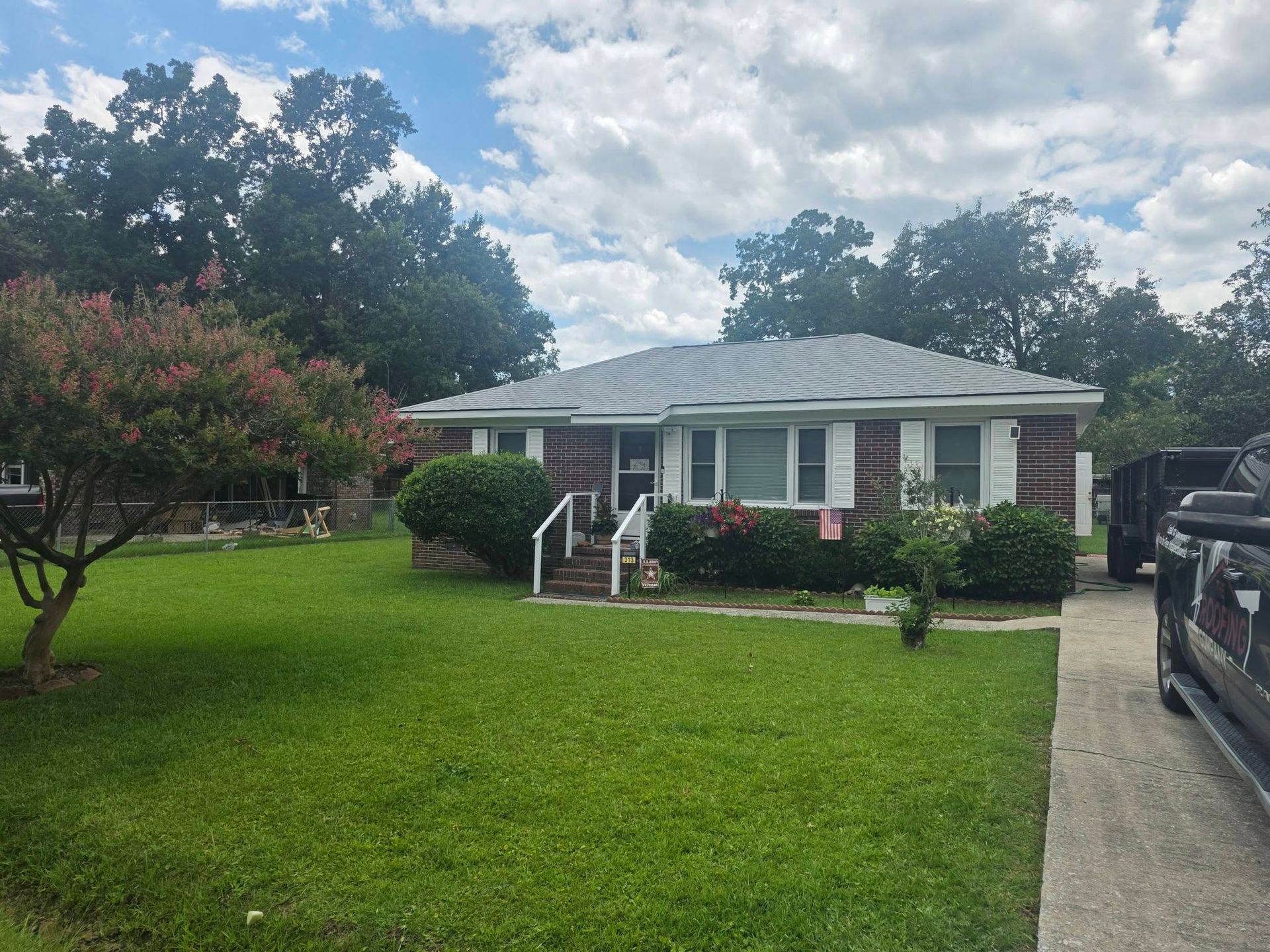 Single-story brick house with white trim, front porch, green lawn, and driveway under a cloudy sky