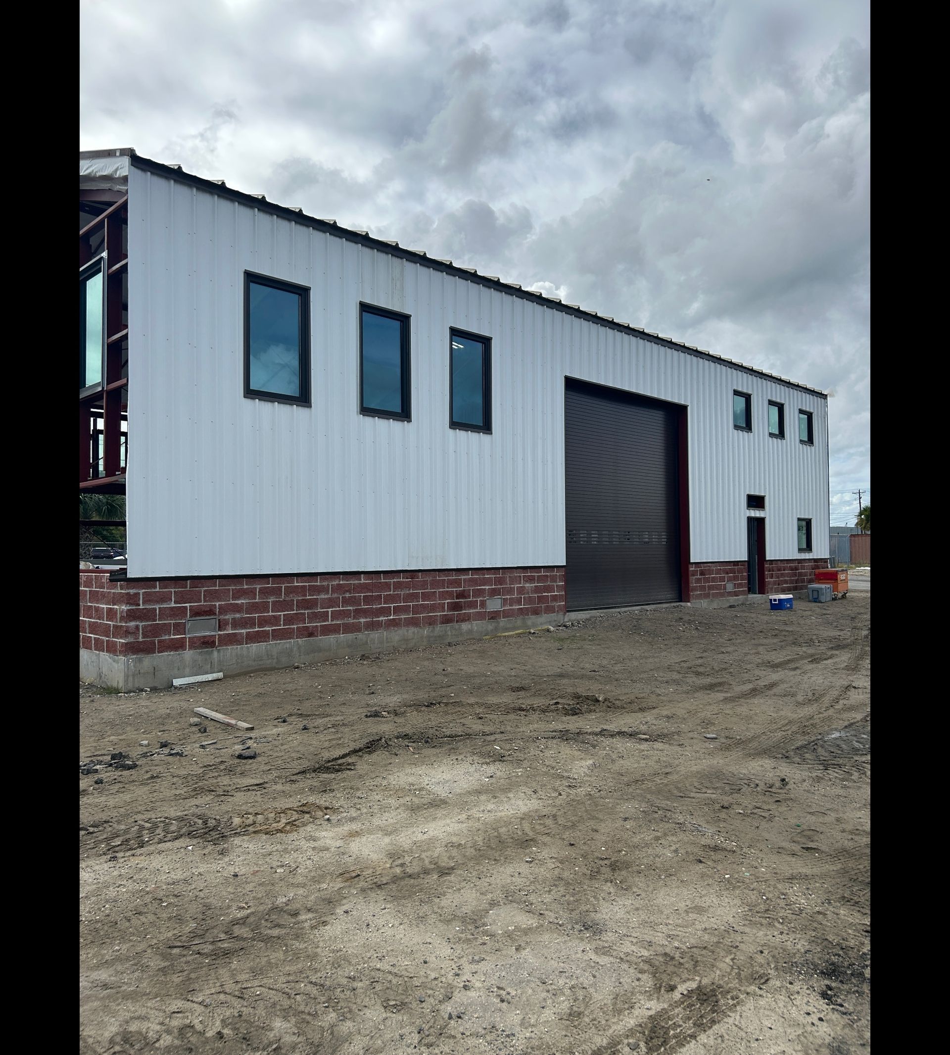 New white metal warehouse with brick base and large roll-up door under cloudy sky