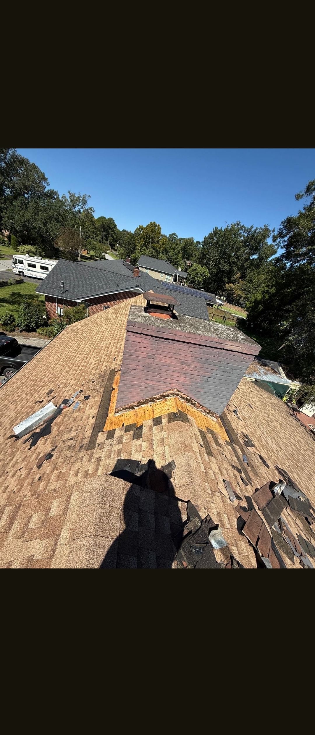 Roofer’s shadow on a steep shingle roof with a damaged section and trees in the background
