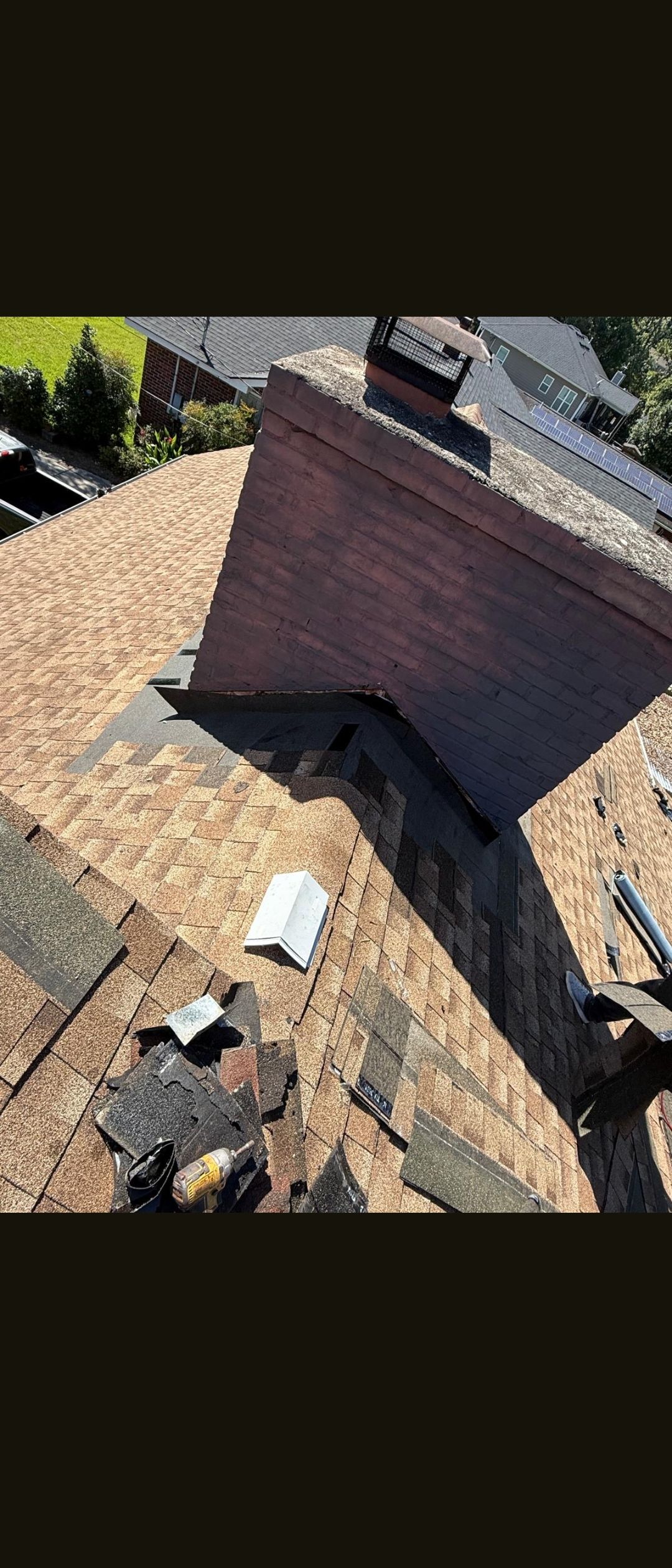 Steep shingled roof with a brick chimney and nearby vent in bright sunlight