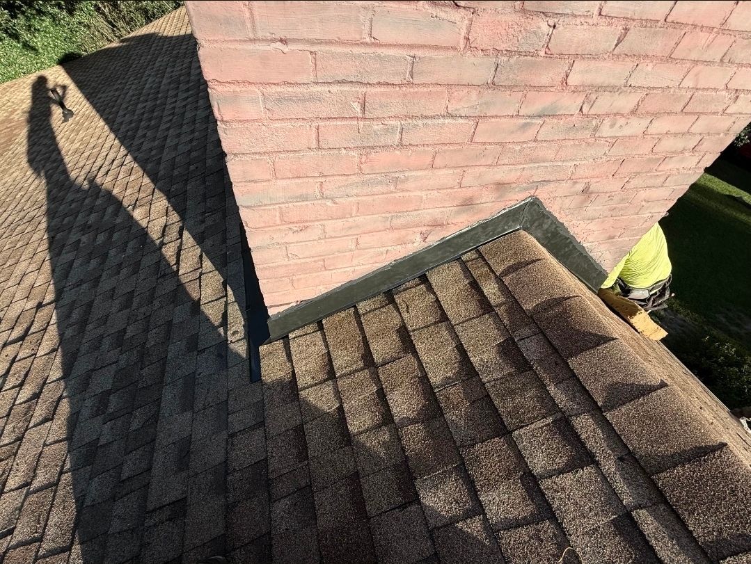 Brick building corner above dark shingled roof in sunlight