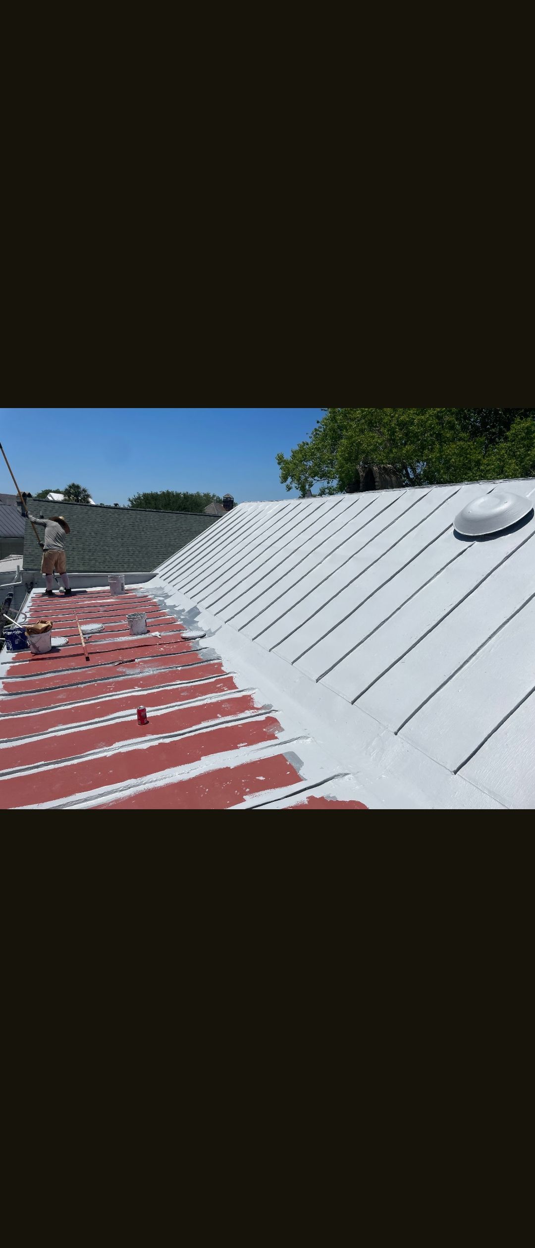 Partly painted corrugated metal roof with red primer and white coating under a blue sky