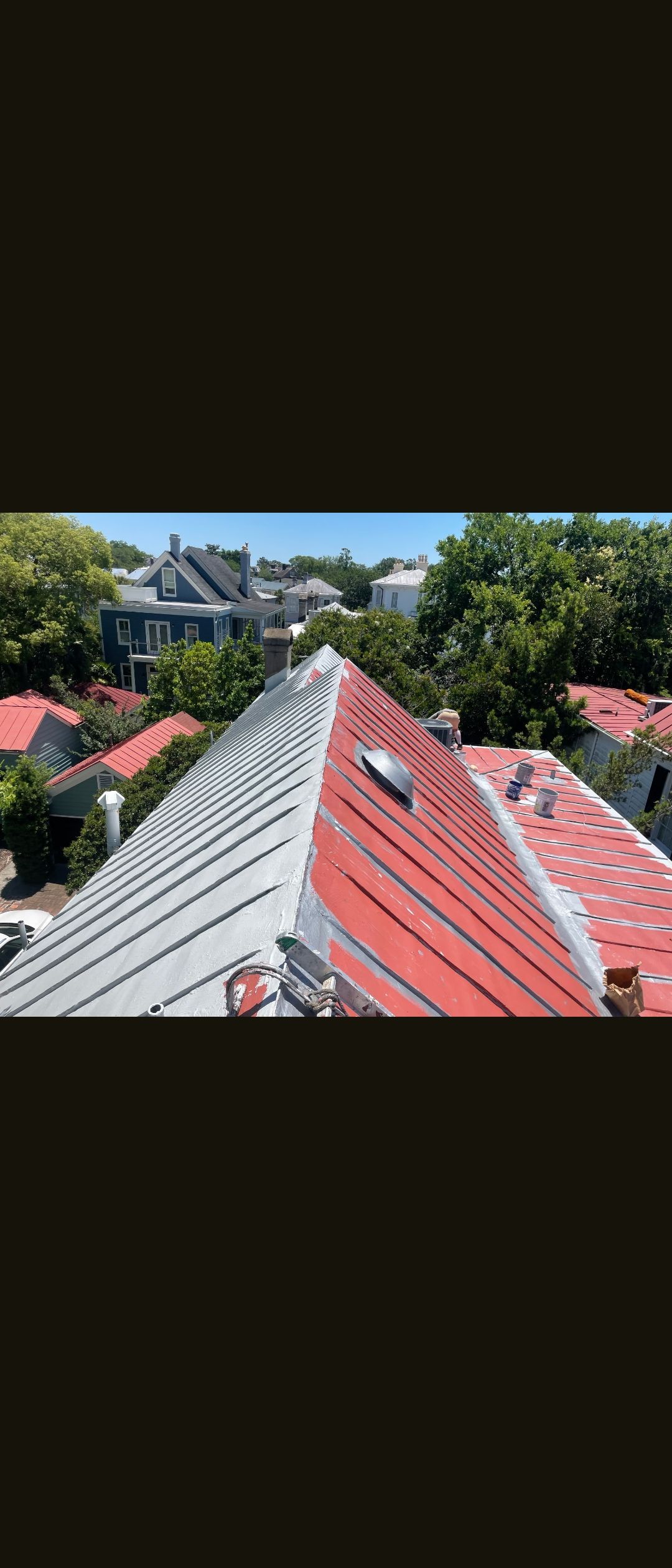 Red-tiled rooftop view toward houses and trees under a clear blue sky