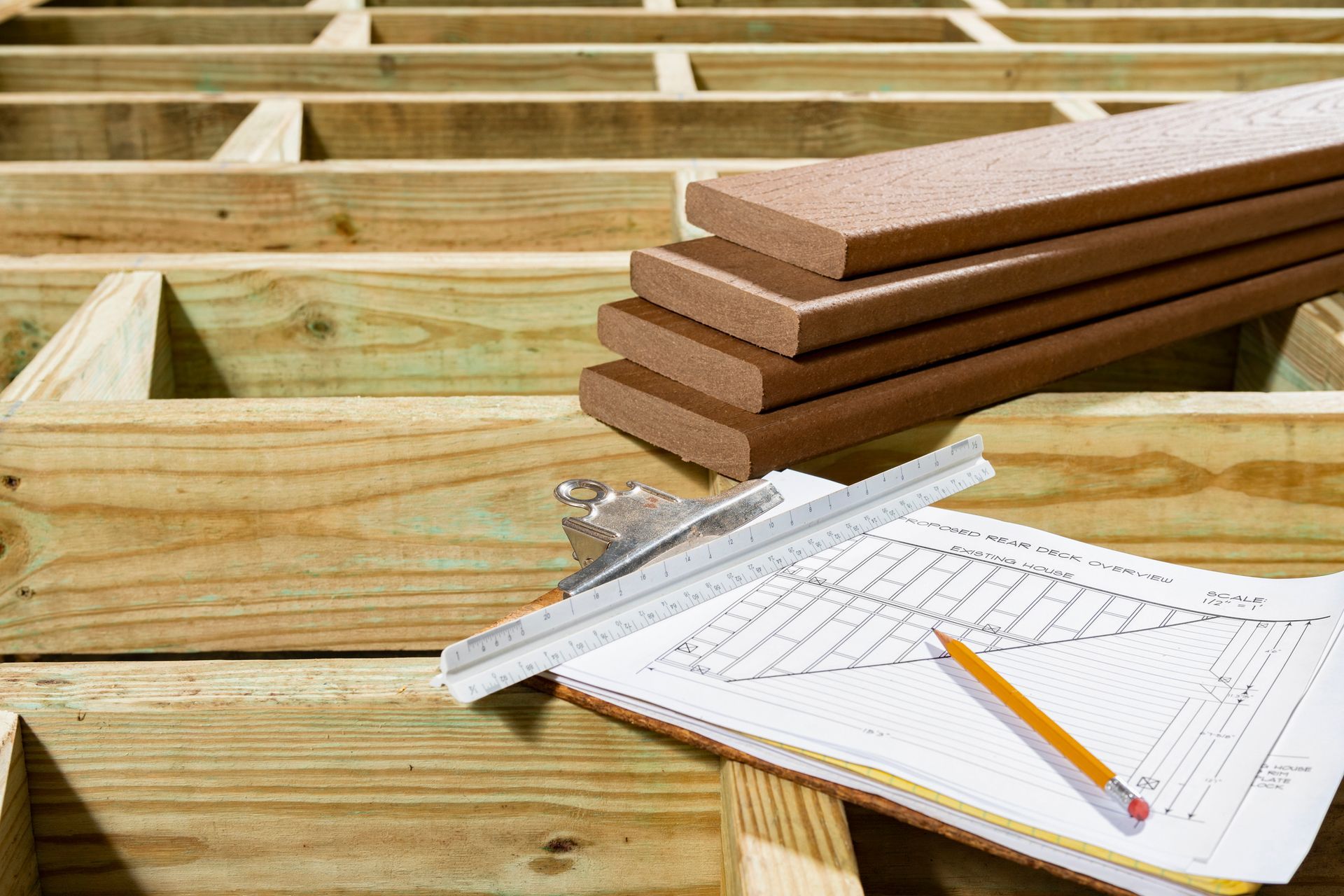 Wooden deck frame with stacked boards, blueprint, pencil, and ruler on a construction site