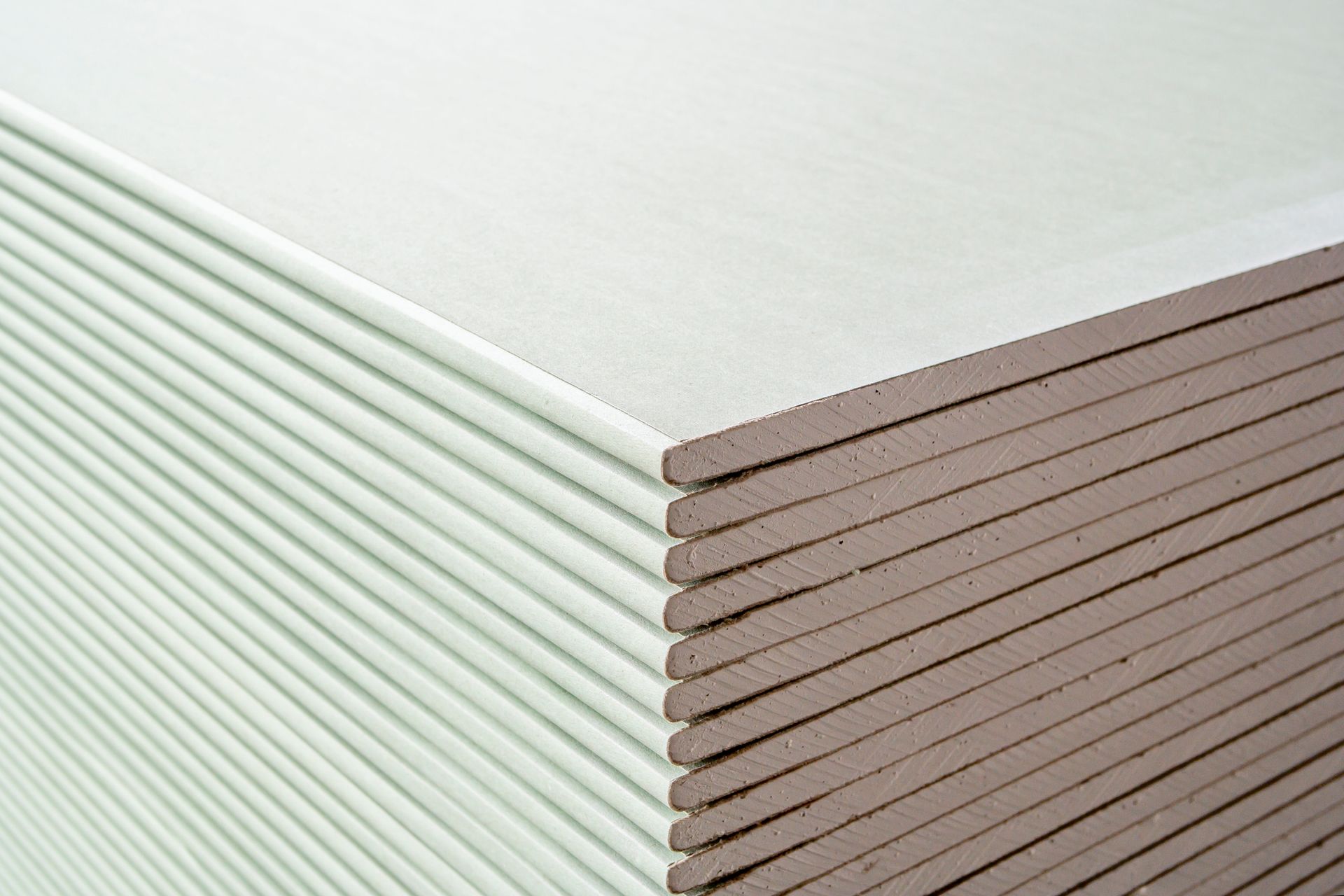 Stack of drywall sheets, light green paper on one side, brown on the other.