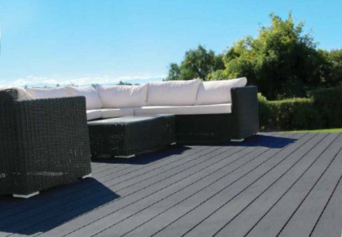 Dark gray composite deck with black wicker patio furniture and white cushions, on a sunny day.