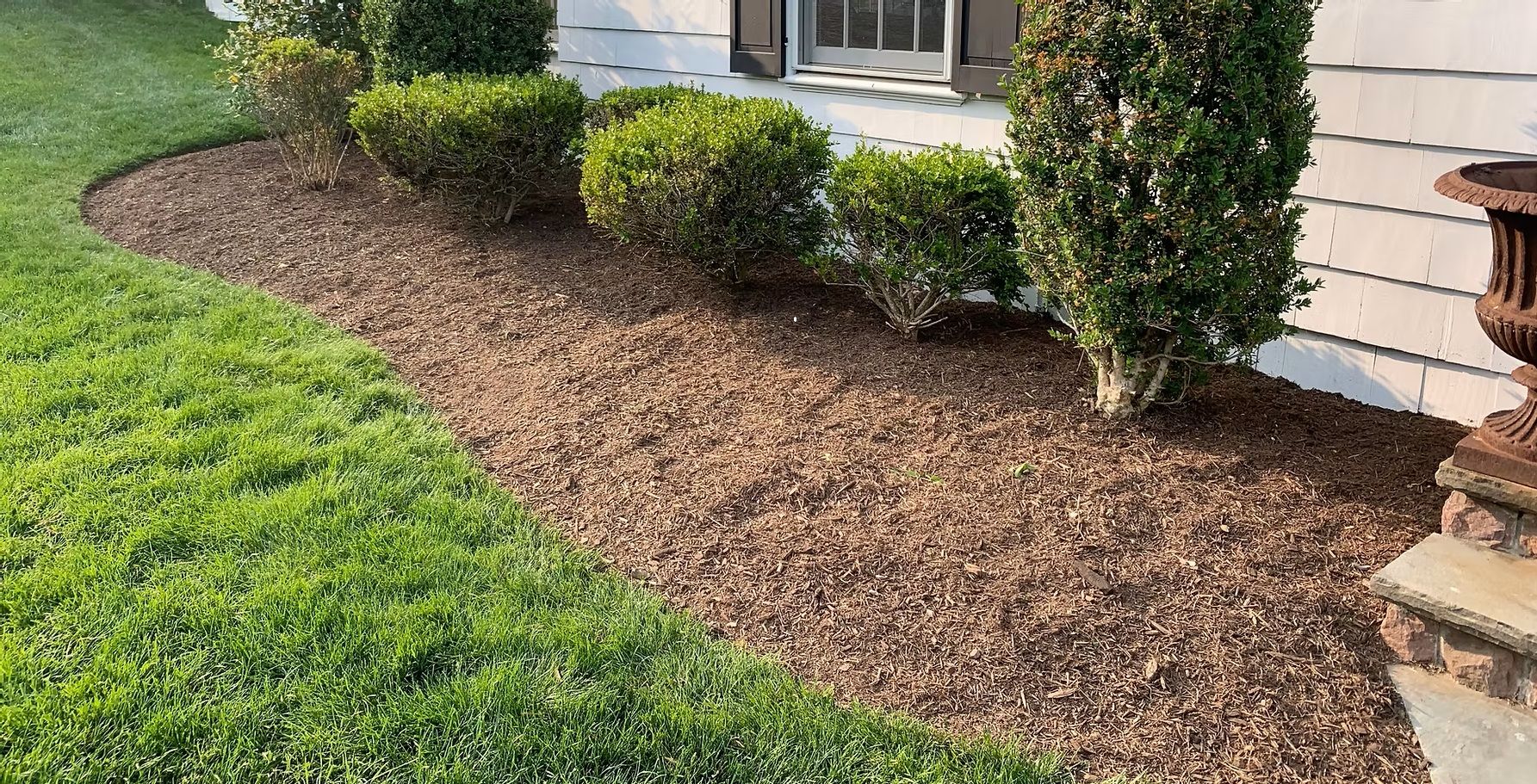 Mulched landscape bed with green shrubs beside a house and lawn