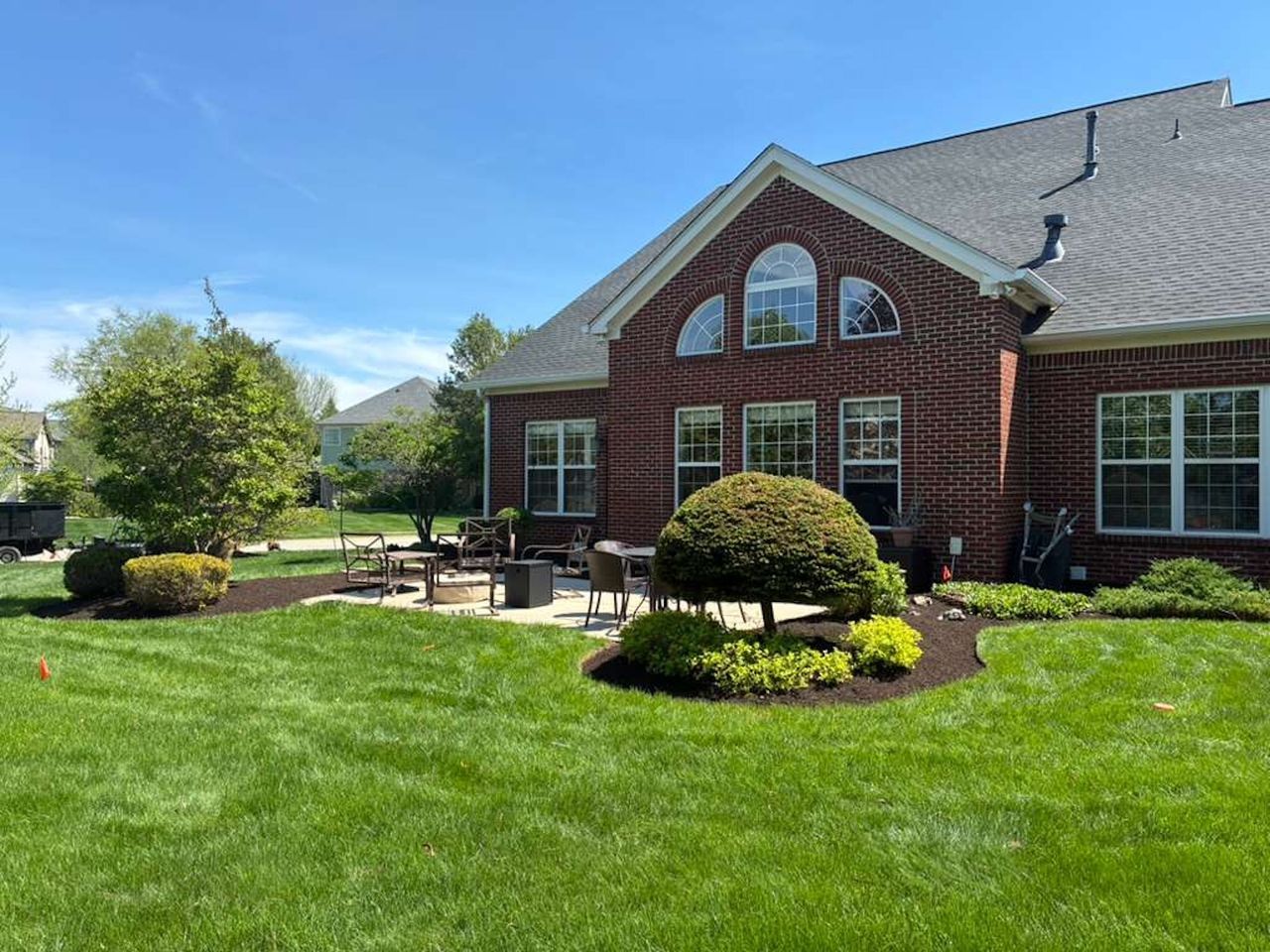 Brick suburban house with manicured lawn, trimmed shrubs, and a patio under a clear blue sky
