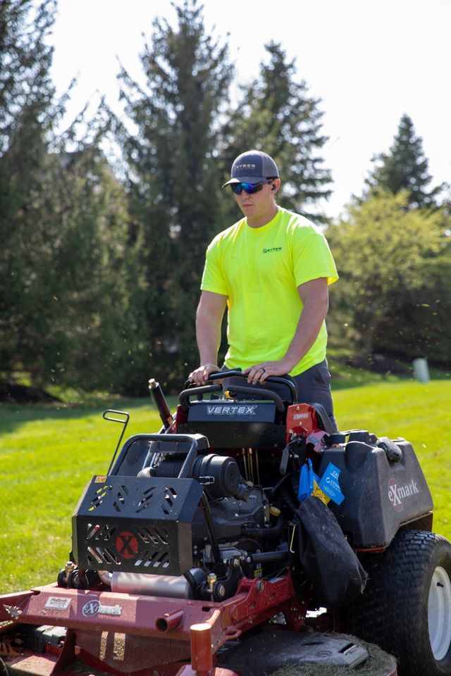 Person in neon yellow shirt riding a red lawn mower on grass outdoors