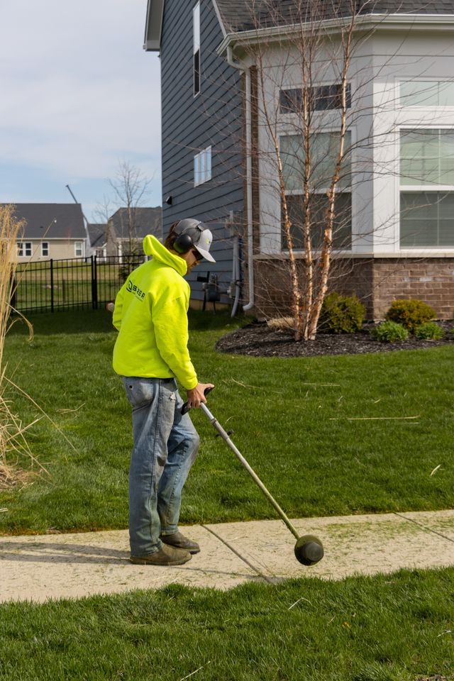 Person in a neon jacket golfing on a sidewalk beside a suburban house
