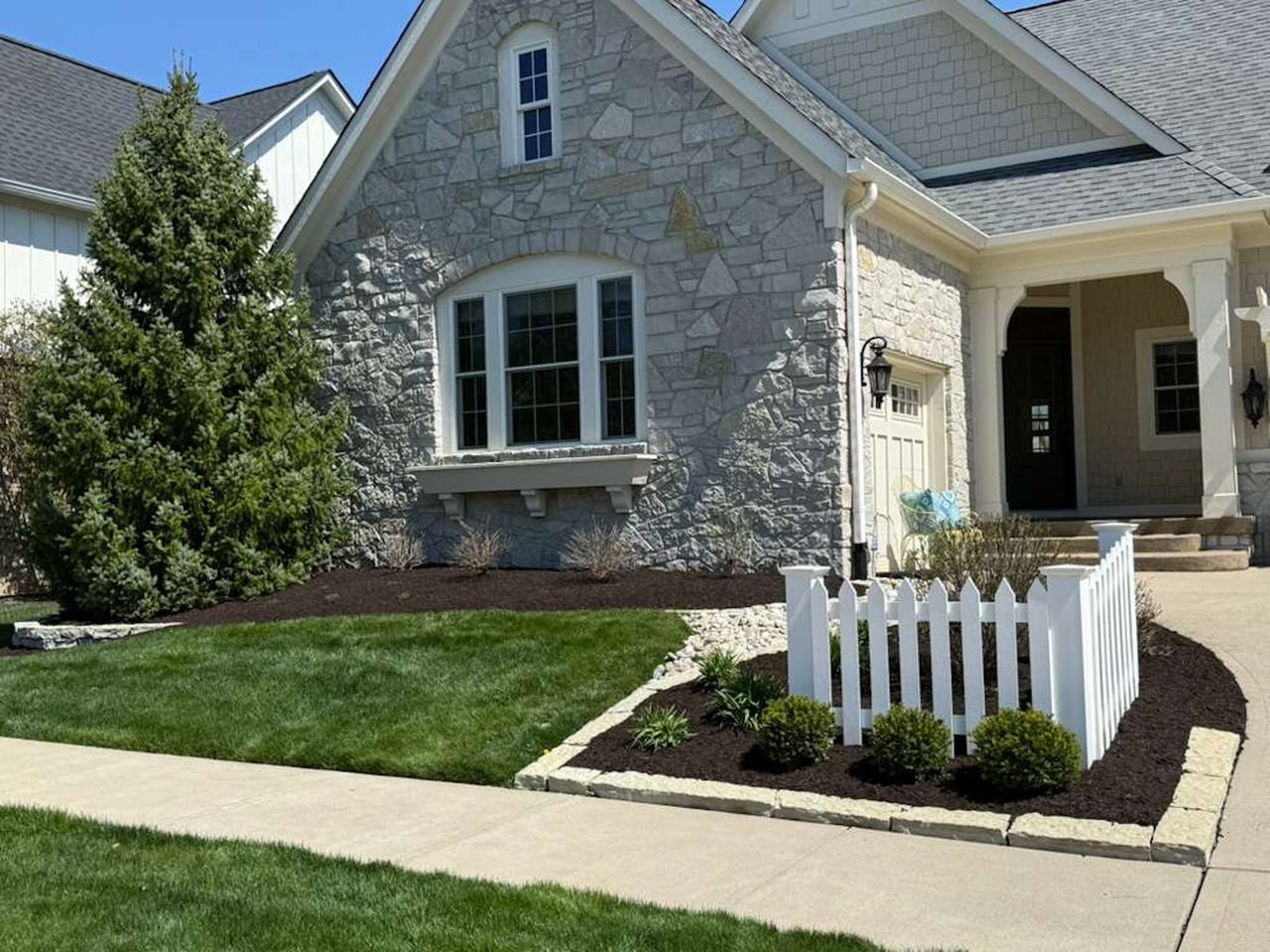 Stone house with manicured lawn, white picket fence, and front porch in bright sunlight