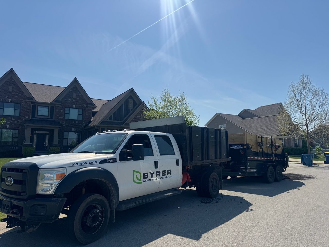 White utility truck with trailer parked on a suburban street in bright sunlight