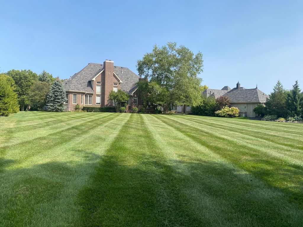 Large brick house with a manicured striped lawn and trees under a clear blue sky