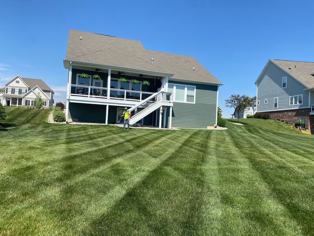 Backyard with a large green lawn, a house, and a deck under a clear blue sky.