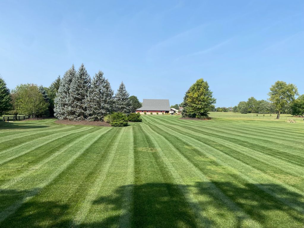 Wide striped green lawn with trees and a small barn under a clear blue sky