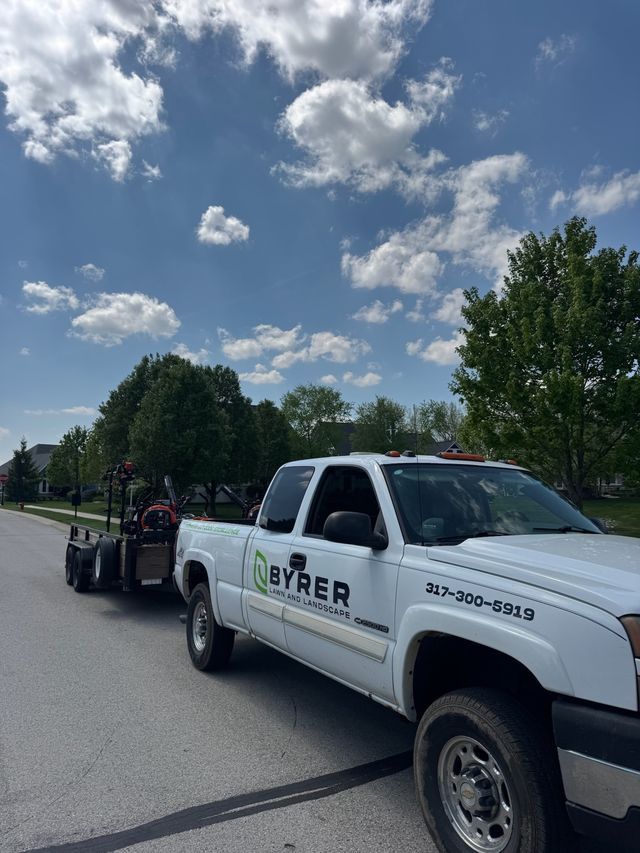 White BYRER pickup truck towing a small trailer on a sunny road under a partly cloudy sky