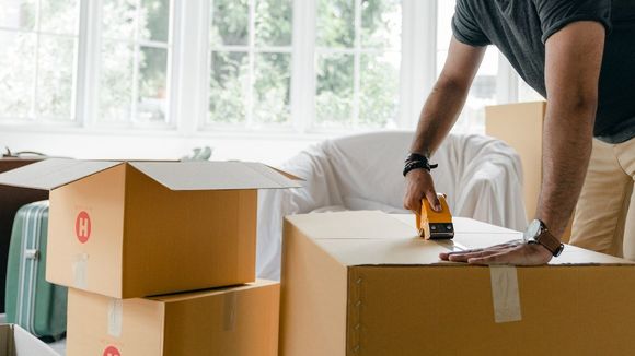 Person packing a cardboard box with a tape gun in a bright room, moving or unpacking boxes.