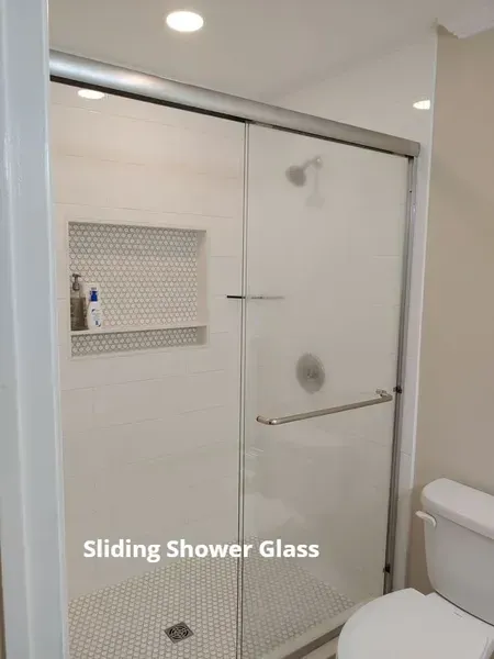 Sliding shower glass door in a modern white bathroom with built-in shelf and grab bar