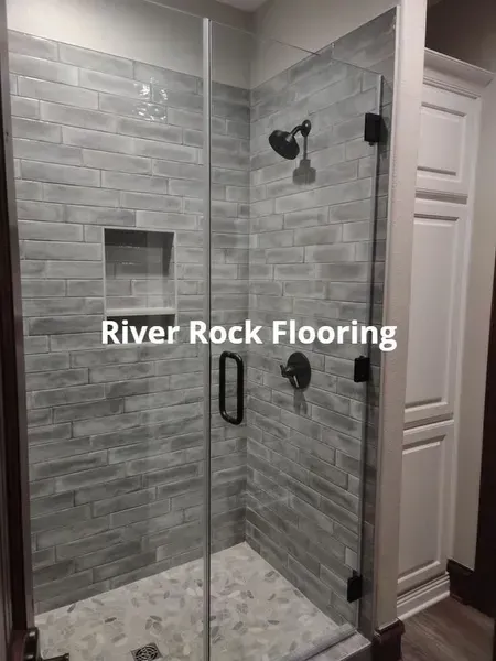 Glass shower enclosure with gray tile walls and mosaic floor in a bathroom