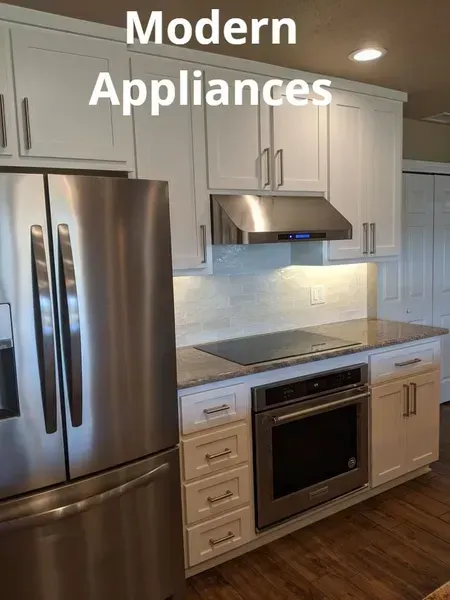 Modern white kitchen with stainless steel refrigerator, oven, and range hood under 