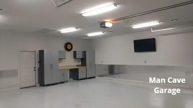 Spacious white garage with cabinets, wall clock, ceiling lights, and a TV on the wall.