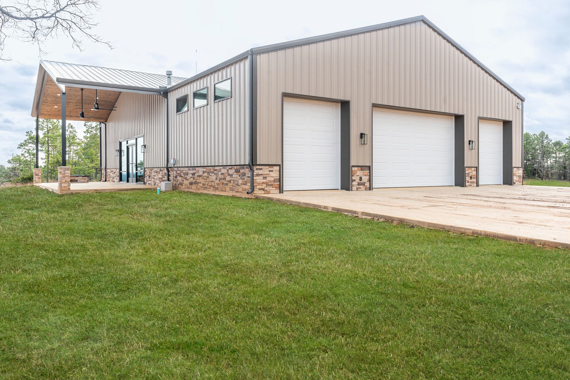 Modern metal garage building with two white doors and a stone base, beside a grassy lawn