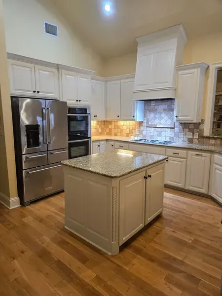 Bright kitchen with white cabinets, stainless appliances, granite island, and hardwood floors.
