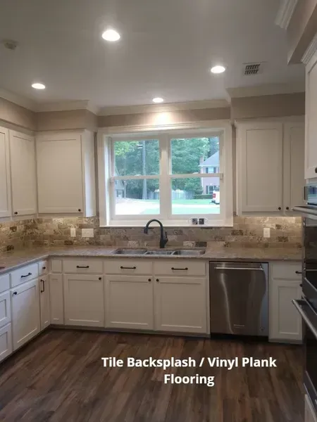 Bright kitchen with white cabinets, tile backsplash, vinyl plank flooring, and a large window over the sink