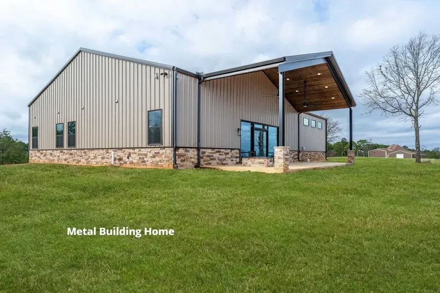 Modern metal building home with stone base, covered porch, and large windows on a grassy lot