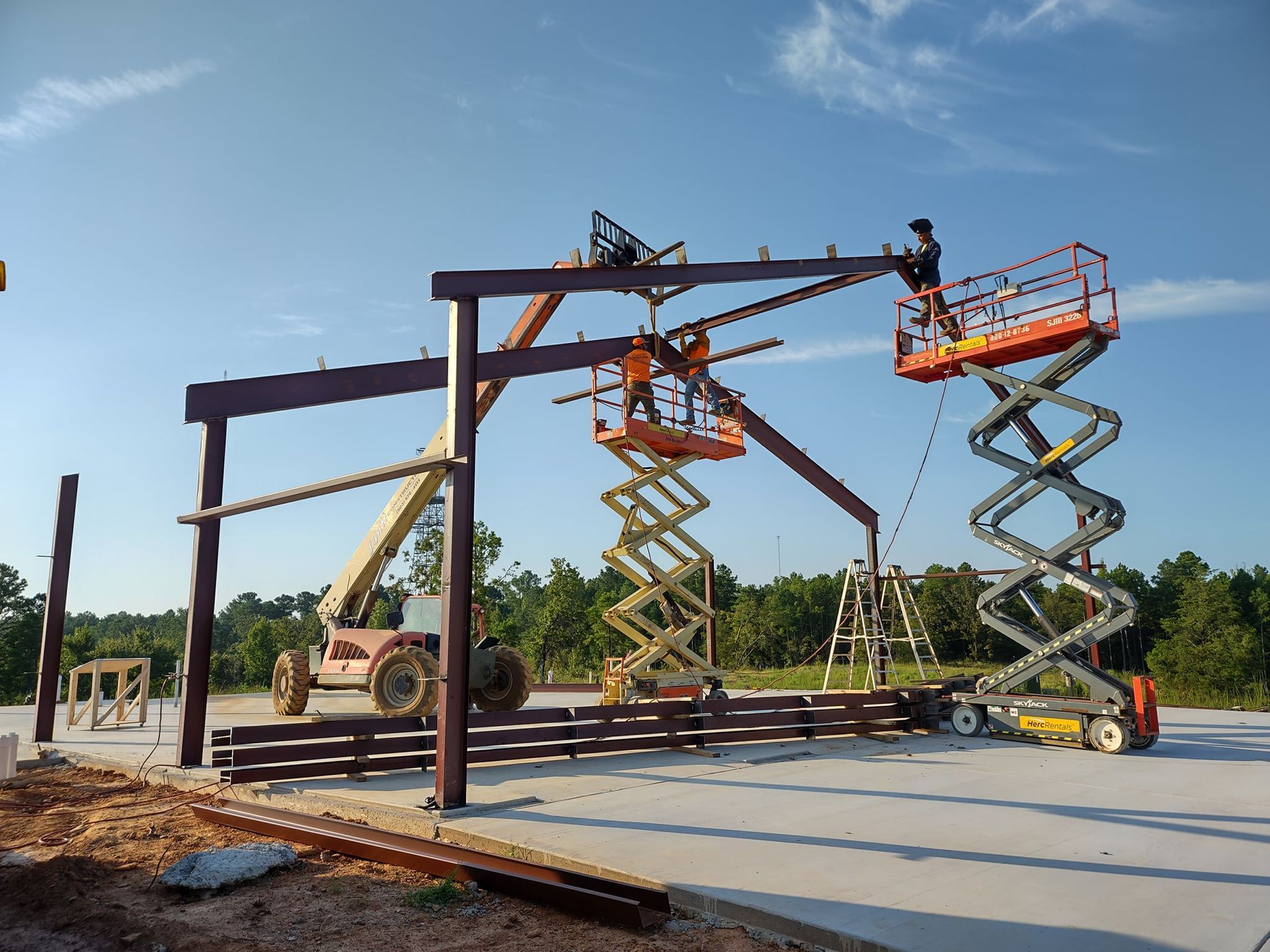Construction workers are working on a metal structure with scissor lifts