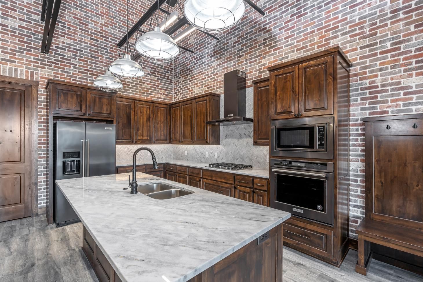 A kitchen with a large island , stainless steel appliances , wooden cabinets and a brick wall.