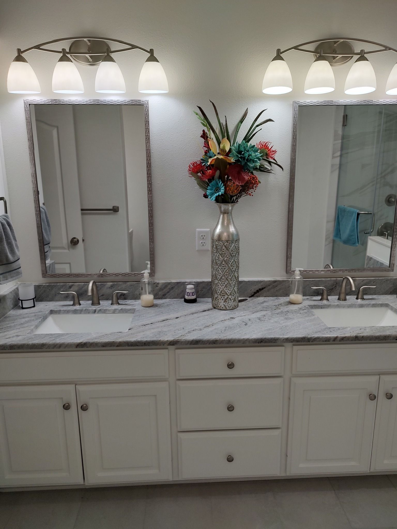 A bathroom with two sinks , two mirrors and a vase of flowers.