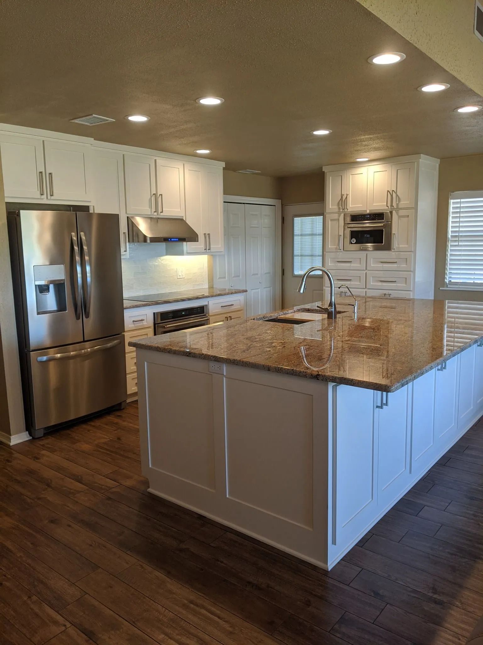 Bright modern kitchen with stainless steel appliances, white cabinets, and a large granite island.