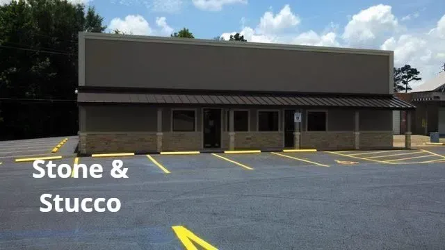 Vacant stone and stucco storefront with yellow parking lines under a partly cloudy sky