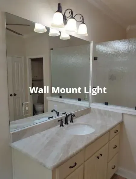 Bathroom vanity with mirror, sink, and frosted glass shower door, lit by a wall-mounted light fixture.
