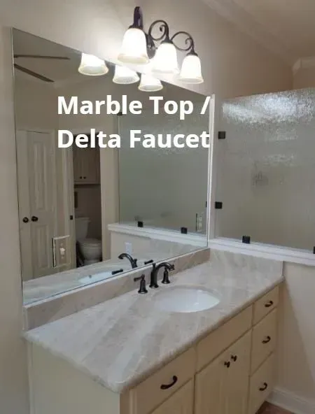 Bathroom vanity with marble countertop, sink, mirror, and dark faucet.