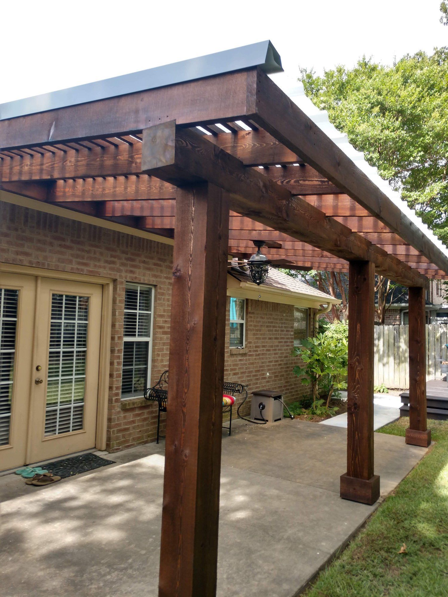 A wooden pergola is sitting in front of a brick house.